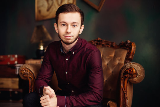 stylish young man in burgundy shirt sitting in luxury armchair a