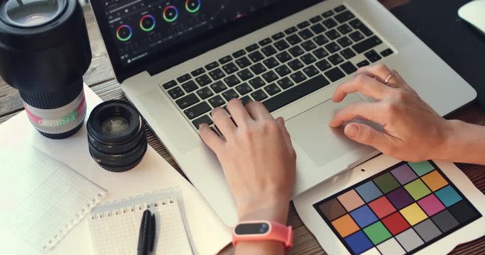 Back view of female video editor works with footage on laptop at home