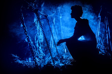 Silhouette of a mysterious witch on the suspension bridge with clouds of smoke around her.