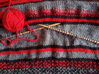 Red yarn ball, knitted wool garment and wooden needles for knitting