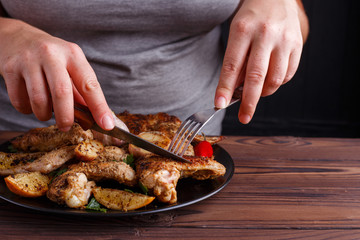 Woman tasting grilled chicken wings with fork and knife. Kitchen