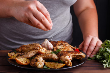 Woman adding salt to grilled chicken wings. Kitchen background,