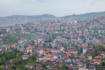 Fototapeta na wymiar Aerial view of the hills of the suburbs of Sarajevo, Bosnia and Herzegovina during a cloudy and rainy day of spring. A mosque can be seen in front.