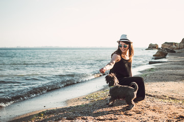Young stylish hipster woman playing with schnauzer dog on the beach