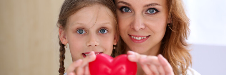 Beautiful smiling woman and kid hold red toy heart
