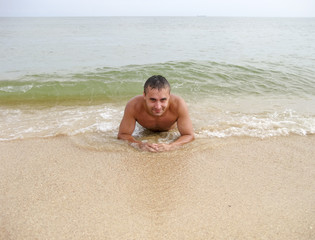 Fototapeta na wymiar man on the shore lies. The sea wave covers the masculine. Beach vacation.