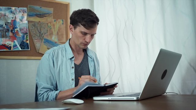 Casual dressed creative man uses laptop in office and draws in sketchpad