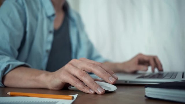 Young guy using laptop in office. Male hands with a wireless mouse