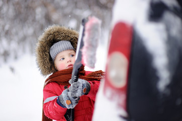 Cute little child helping to brush a snow from a car