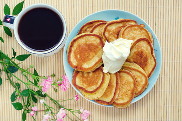 Rustic breakfast - pancakes with coffee and sour cream. Wooden background, rose flower.