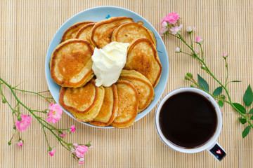 Pancakes on a plate with sour cream, coffee. Wooden background, rose flowers.