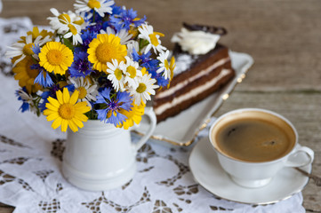 Delicious chocolate cake on a plate with a coffee and bouquet of wildflowers