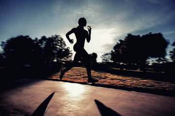 A silhouette of an athlete running on a track behind the sunset.
