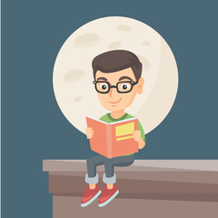 Caucasian boy in glasses sitting on the roof of the house with a book in hands