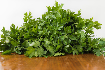 Low angele view of bunch of fresh, wet garden parsley leaves with little imperfections lying on wooden kitchen table with white background