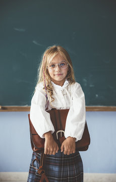 Portrait of girl holding schoolbag while standing in classroom