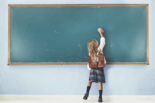 Rear view of little girl cleaning blackboard in classroom