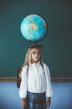 Portrait of girl balancing globe on head in classroom