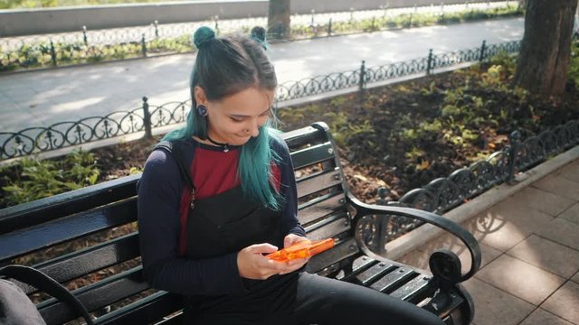 Street punk or hipster girl playing tetris game in European park. Portrait of teen girl with blue dyed hair,piercing in nose,violet lenses and unusual hairstyle.Old school concept. Slow motion.