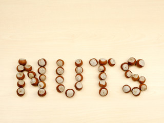 Word NUTS spelled with various nuts on a wooden background.