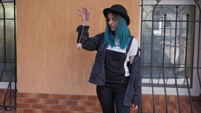 SLOW MOTION: emo girl playing with old school toy yo yo. Street punk or hipster with blue dyed hair,piercing,lenses,tattooed,ears tunnels and unusual hairstyle stands in backyard.