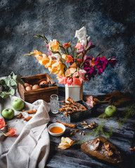 Fototapeta na wymiar cookies in metal box with green apples, honey in small plate, crushed cookie on wooden board, eggs in wooden box, assorted gladiolus flowers in white vase and textile on blue background