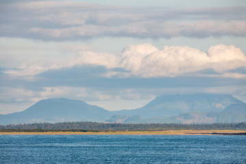 Quiet pacific ocean with mountain shore and white clouds.