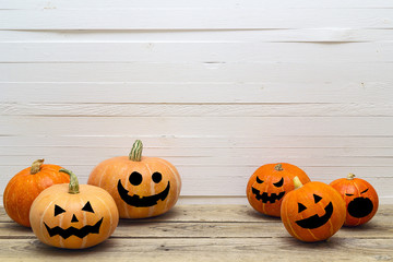 Halloween pumpkins with painted faces on a wooden table on a background of white boards. Space for text.