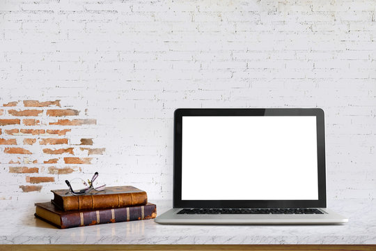 Workspace desk with blank screen laptop, gadget, and vintage books with copy space on white brick wall.
