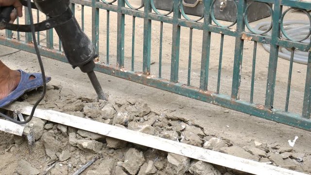 Worker breaking cement floor by using demolition hammer