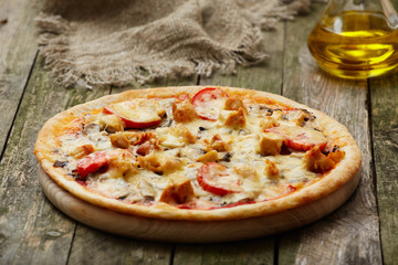 Chicken pizza and oil on a rustic wooden table. Selective focus.