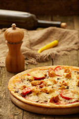 Chicken pizza pepper mill, yellow chili and wine bottle on a rustic wooden table. Selective focus.