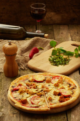 Chicken pizza pepper mill, chili, sliced greenery, sweet pepper and wine bottle on a rustic wooden table. Selective focus.
