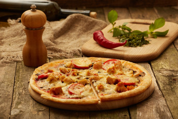 Chicken pizza pepper mill, chili,  and wine bottle on a rustic wooden table. Selective focus.