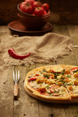 Chicken pizza pepper mill, chili, fork, and wine bottle on a rustic wooden table. Selective focus.