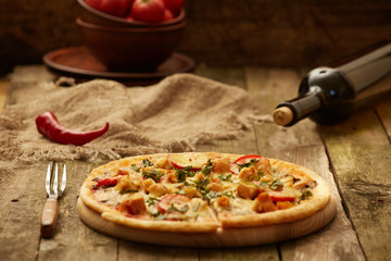 Chicken pizza pepper mill, chili, fork  and wine bottle on a rustic wooden table. Selective focus.