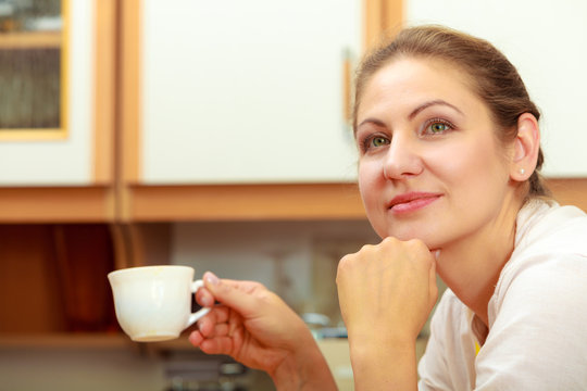 Mature woman holding cup of coffee in kitchen.
