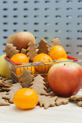 Apple, mandarins, christmas cookies in the shopping cart on the grey background