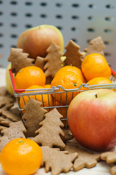 Apple, mandarins, christmas cookies in the shopping cart on the grey background