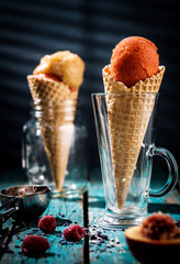 Different sorts of sorbet in waffle cones on a wooden table.