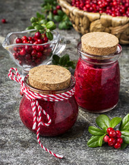 Puree of the northern wild forest cowberry, cranberry for a healthy organic diet in small glass portioned jars with berries and leaves on a gray stone background. Selective focus.
