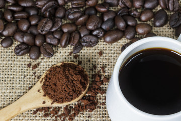 Coffee grind in wooden spoon and hot coffee on sackcloth with coffee beans background.