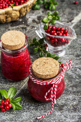 Puree of the northern wild forest cowberry, cranberry for a healthy organic diet in small glass portioned jars with berries and leaves on a gray stone background. Selective focus.