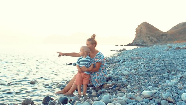 Evening, sea beach. The son sits on his mother's lap and eats fruit and berries