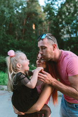 Young family portrait, mother, father and daughter having fun together and hug each other. They blow on a dandelion