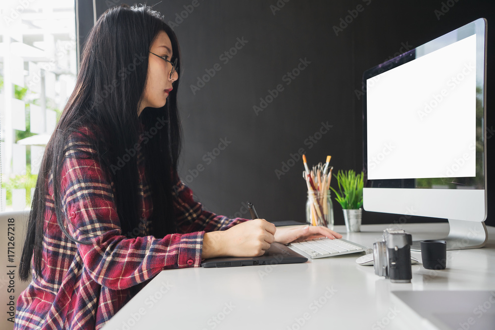 Fototapete Young asian female designer using graphics tablet while working with computer at studio or office.