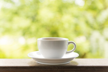Fototapeta na wymiar White ceramic tea cup on wooden table on green background