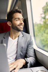 Handsome guy on train using laptop, smiling