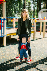 Young mother with her beautiful son stands at the playground. Outdoors healthy child activity, active lifestyle and having fun on family summer vacation with son at the playground