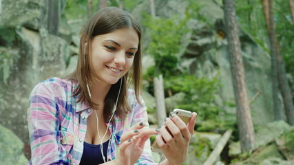 A young woman tourist uses a smartphone in a hike. Sits resting against the rocks in the mountains